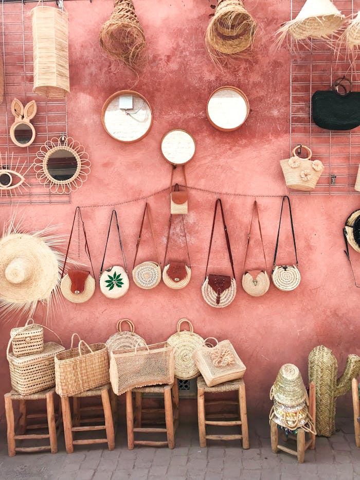 Aesthetic display of handmade wicker and straw accessories against a textured pink wall.